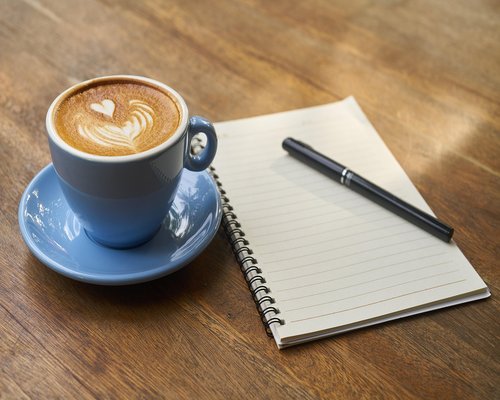 A notebook and pen resting on a modern desk next to a coffee cup